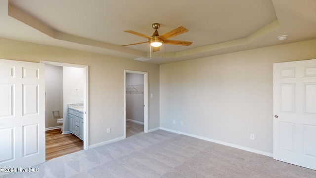 unfurnished bedroom with a spacious closet, light carpet, ceiling fan, a tray ceiling, and a closet