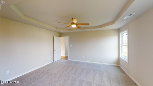 carpeted spare room featuring ceiling fan and a tray ceiling