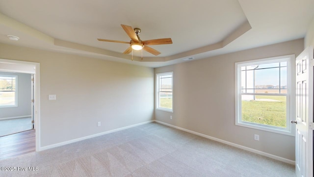 carpeted spare room with ceiling fan, a wealth of natural light, and a tray ceiling