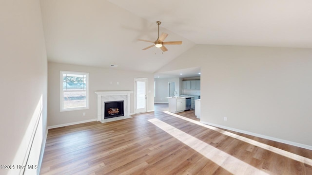 unfurnished living room with lofted ceiling, a fireplace, light hardwood / wood-style floors, sink, and ceiling fan