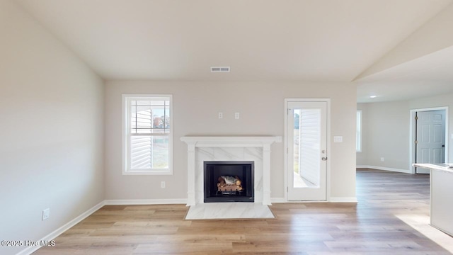 unfurnished living room with lofted ceiling, a tiled fireplace, and light wood-type flooring