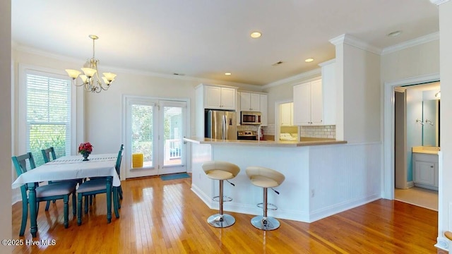 kitchen featuring appliances with stainless steel finishes, white cabinetry, decorative backsplash, ornamental molding, and kitchen peninsula