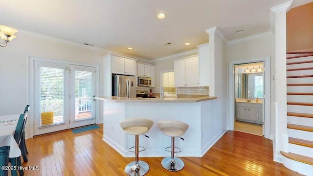 kitchen featuring tasteful backsplash, kitchen peninsula, a kitchen bar, stainless steel appliances, and white cabinets