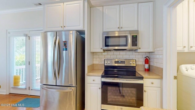 kitchen featuring washer / dryer, white cabinetry, appliances with stainless steel finishes, tasteful backsplash, and crown molding