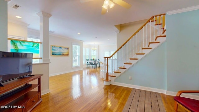 interior space featuring crown molding, ceiling fan with notable chandelier, hardwood / wood-style floors, and decorative columns