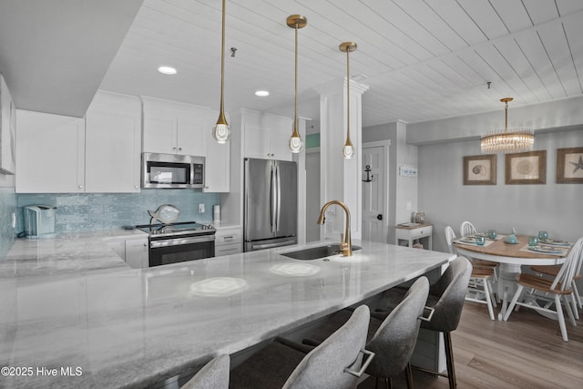 kitchen with appliances with stainless steel finishes, backsplash, hanging light fixtures, white cabinets, and sink