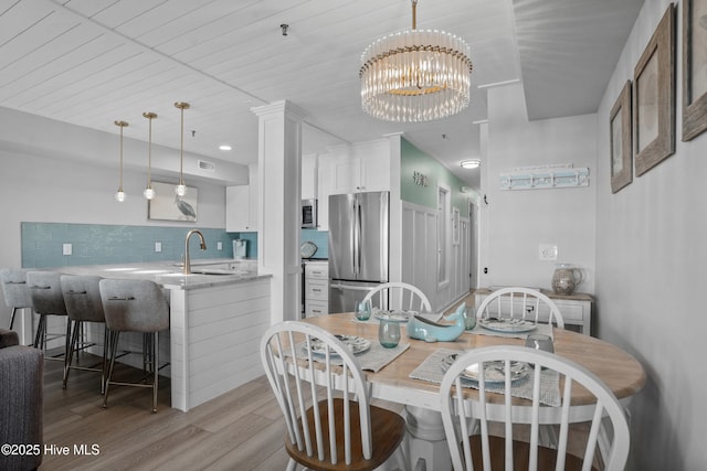 dining room featuring sink, an inviting chandelier, wooden ceiling, light wood-type flooring, and ornate columns