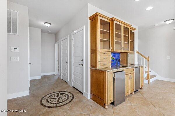 kitchen with light tile patterned flooring, light stone countertops, and refrigerator