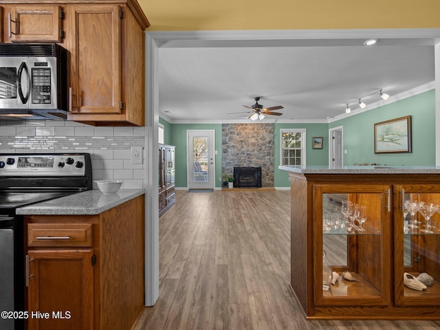 kitchen with appliances with stainless steel finishes, a stone fireplace, decorative backsplash, ceiling fan, and light hardwood / wood-style flooring