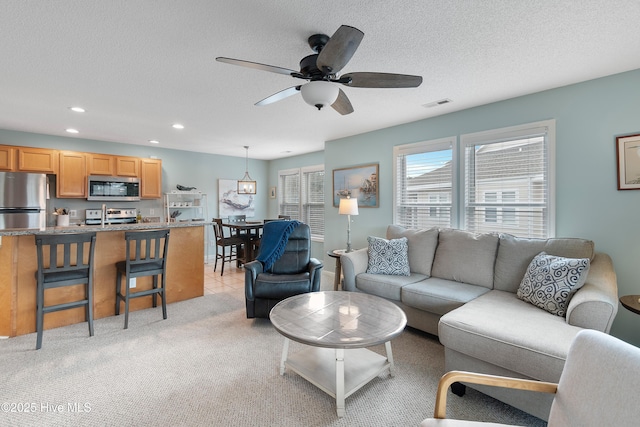 carpeted living room featuring ceiling fan and a textured ceiling