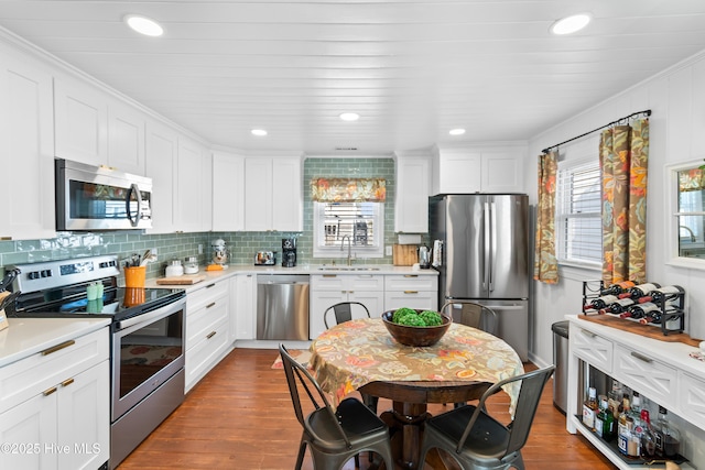 kitchen with appliances with stainless steel finishes, decorative backsplash, wood-type flooring, white cabinets, and sink