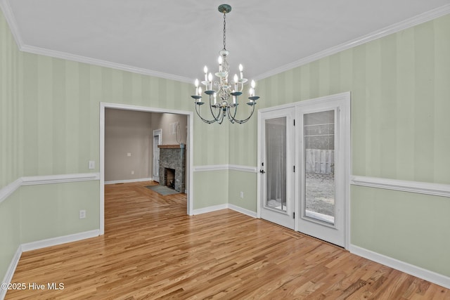 unfurnished dining area with an inviting chandelier, a stone fireplace, wood-type flooring, and ornamental molding