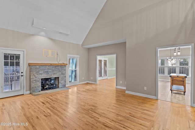 unfurnished living room with a stone fireplace, high vaulted ceiling, a chandelier, and light wood-type flooring