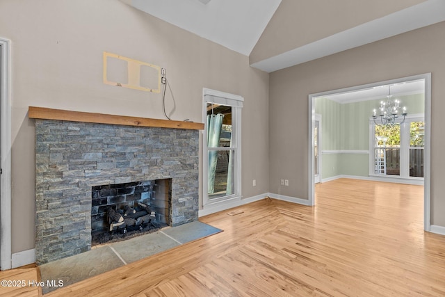 unfurnished living room with lofted ceiling, hardwood / wood-style floors, a stone fireplace, and a chandelier