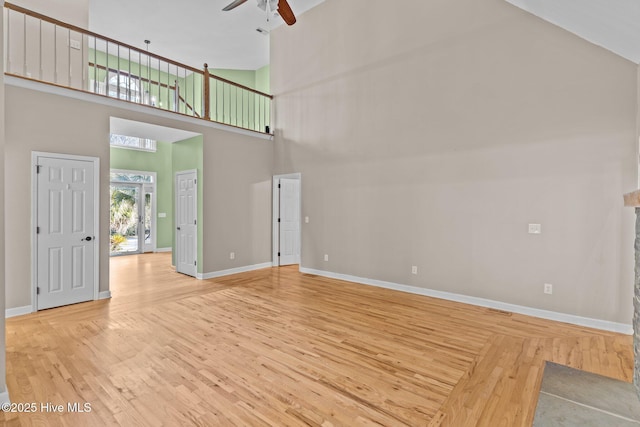 unfurnished living room with ceiling fan, hardwood / wood-style floors, and a high ceiling