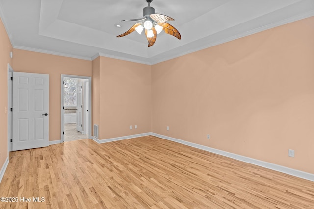 empty room featuring crown molding, ceiling fan, a tray ceiling, and light wood-type flooring