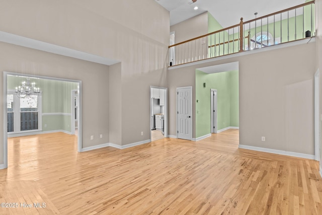 unfurnished living room featuring a towering ceiling, an inviting chandelier, and light hardwood / wood-style floors