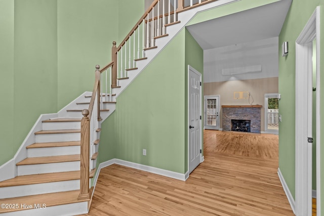 stairway with a high ceiling, a stone fireplace, and hardwood / wood-style floors