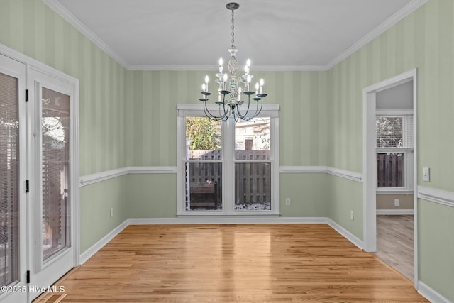 unfurnished dining area with hardwood / wood-style flooring, crown molding, and an inviting chandelier