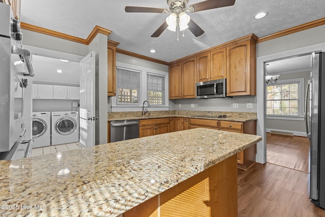 kitchen with sink, ornamental molding, independent washer and dryer, stainless steel appliances, and light stone countertops