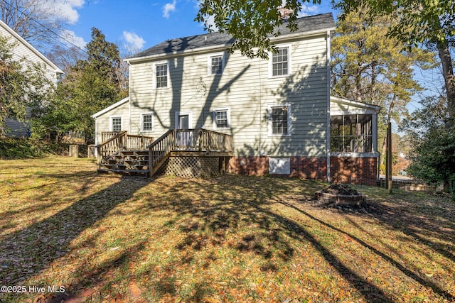 back of property with a sunroom, a yard, a deck, and a fire pit