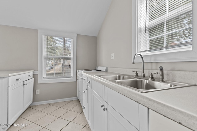 kitchen with light tile patterned flooring, lofted ceiling, sink, white cabinetry, and stove