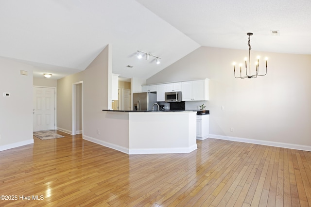 kitchen featuring white cabinets, appliances with stainless steel finishes, light wood-type flooring, hanging light fixtures, and vaulted ceiling