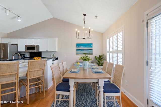 dining room featuring an inviting chandelier, light hardwood / wood-style flooring, and vaulted ceiling