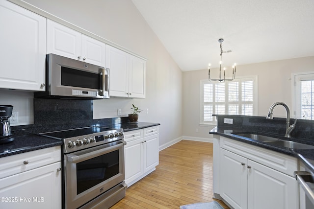 kitchen with hanging light fixtures, appliances with stainless steel finishes, sink, white cabinets, and lofted ceiling