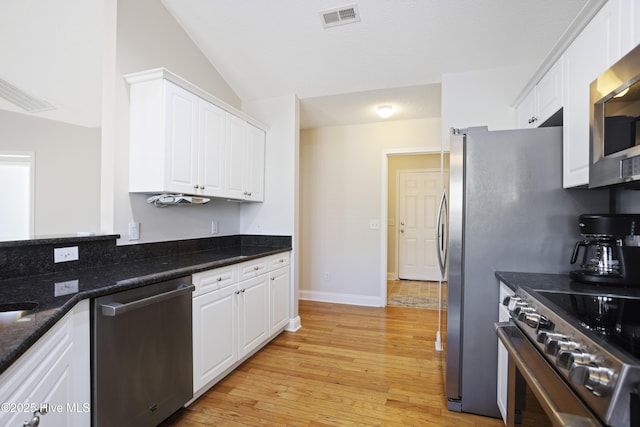 kitchen featuring vaulted ceiling, appliances with stainless steel finishes, light wood-type flooring, white cabinetry, and dark stone countertops