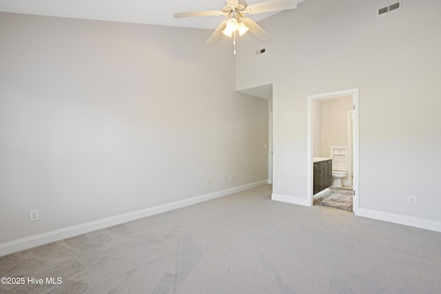 unfurnished bedroom featuring ceiling fan, ensuite bathroom, a towering ceiling, and light carpet