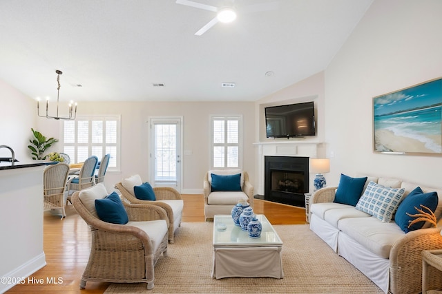 living room featuring vaulted ceiling, ceiling fan with notable chandelier, and light hardwood / wood-style flooring