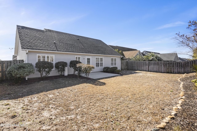 back of property with fence, a shingled roof, and a patio area