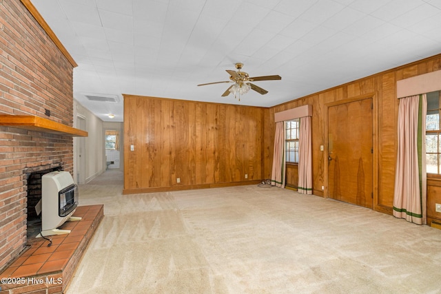 unfurnished living room with wood walls, heating unit, light carpet, and ceiling fan