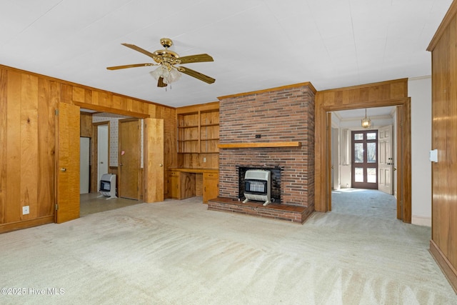 unfurnished living room featuring light carpet, wooden walls, a wood stove, built in features, and ornamental molding