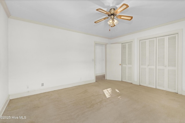 unfurnished bedroom featuring ceiling fan, two closets, light colored carpet, and crown molding