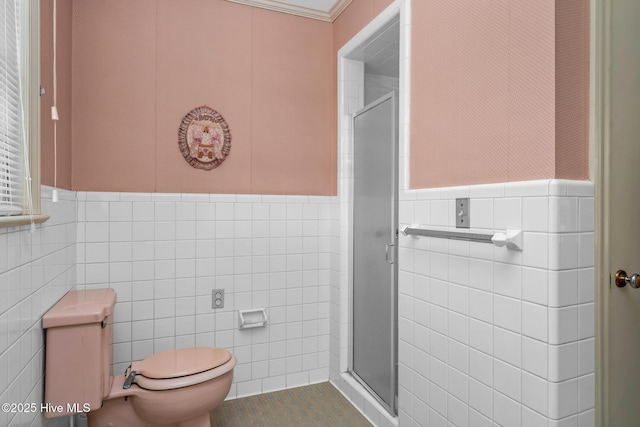 bathroom featuring tile walls, toilet, a shower with door, and crown molding