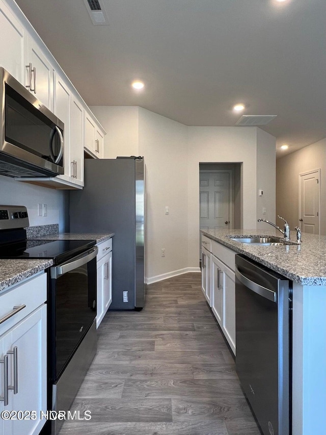 kitchen with dark wood-type flooring, sink, appliances with stainless steel finishes, a kitchen island with sink, and white cabinets