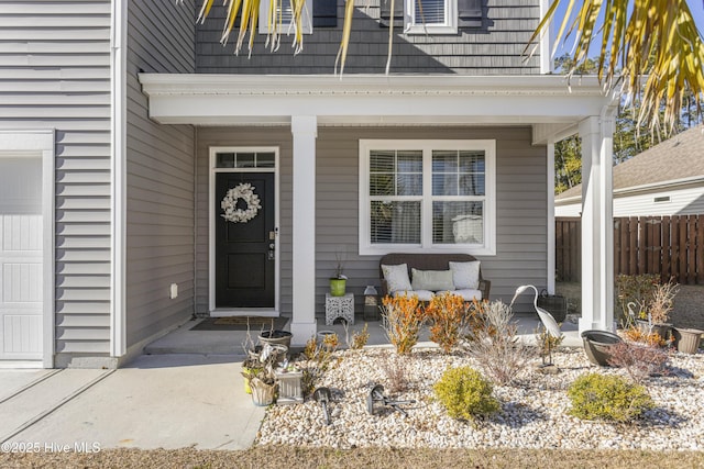 view of exterior entry with a garage, covered porch, and fence