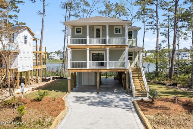 raised beach house with a shingled roof, covered porch, stairway, concrete driveway, and a carport