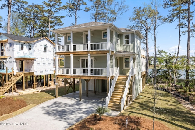 raised beach house with stairs, a porch, a balcony, a carport, and driveway