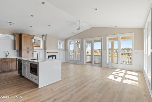 kitchen with brown cabinetry, vaulted ceiling, a sink, light countertops, and a wainscoted wall