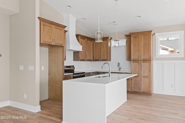 kitchen with stainless steel range with electric cooktop, a sink, light countertops, light wood-style flooring, and a center island with sink