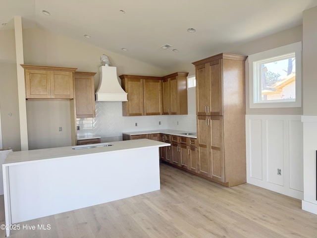 kitchen with light wood finished floors, tasteful backsplash, custom range hood, vaulted ceiling, and a kitchen island