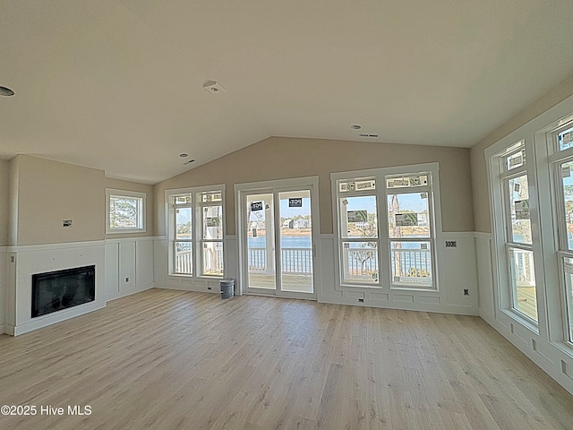 unfurnished living room featuring vaulted ceiling, a glass covered fireplace, light wood-style flooring, and a decorative wall