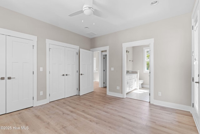 unfurnished bedroom featuring a sink, light wood finished floors, ensuite bath, two closets, and baseboards