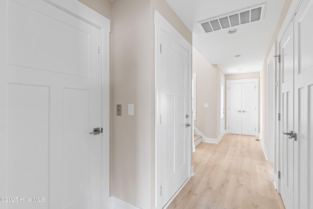 hall with visible vents, baseboards, and light wood-type flooring
