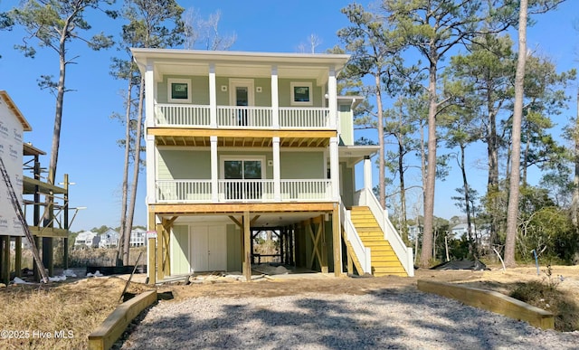 coastal home with covered porch, an outdoor structure, stairs, driveway, and a carport