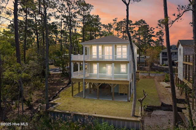 back of property at dusk with a lawn, a carport, a balcony, a patio, and a shingled roof