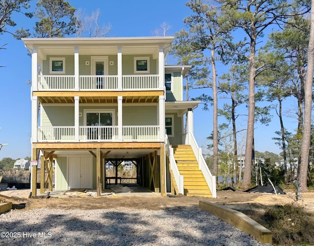 raised beach house with gravel driveway, covered porch, a carport, stairs, and board and batten siding